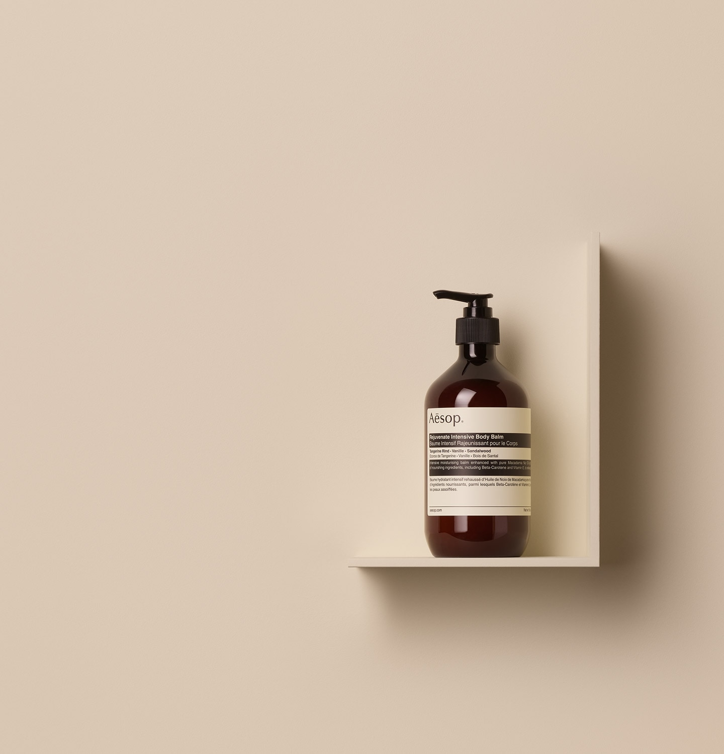 Aesop Rejuvenate Intensive Body Balm in 500ml amber pump bottle, placed on a shelf in a beige surface