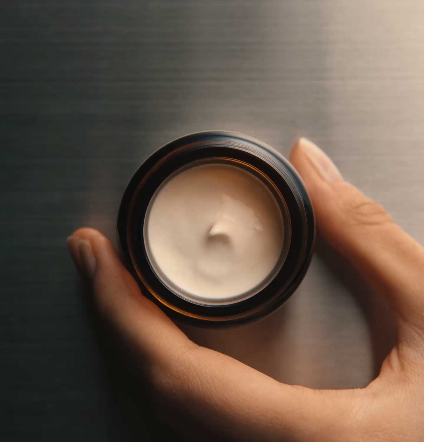 Hand holding an amber glass jar full of Mandarin facial hydrating cream