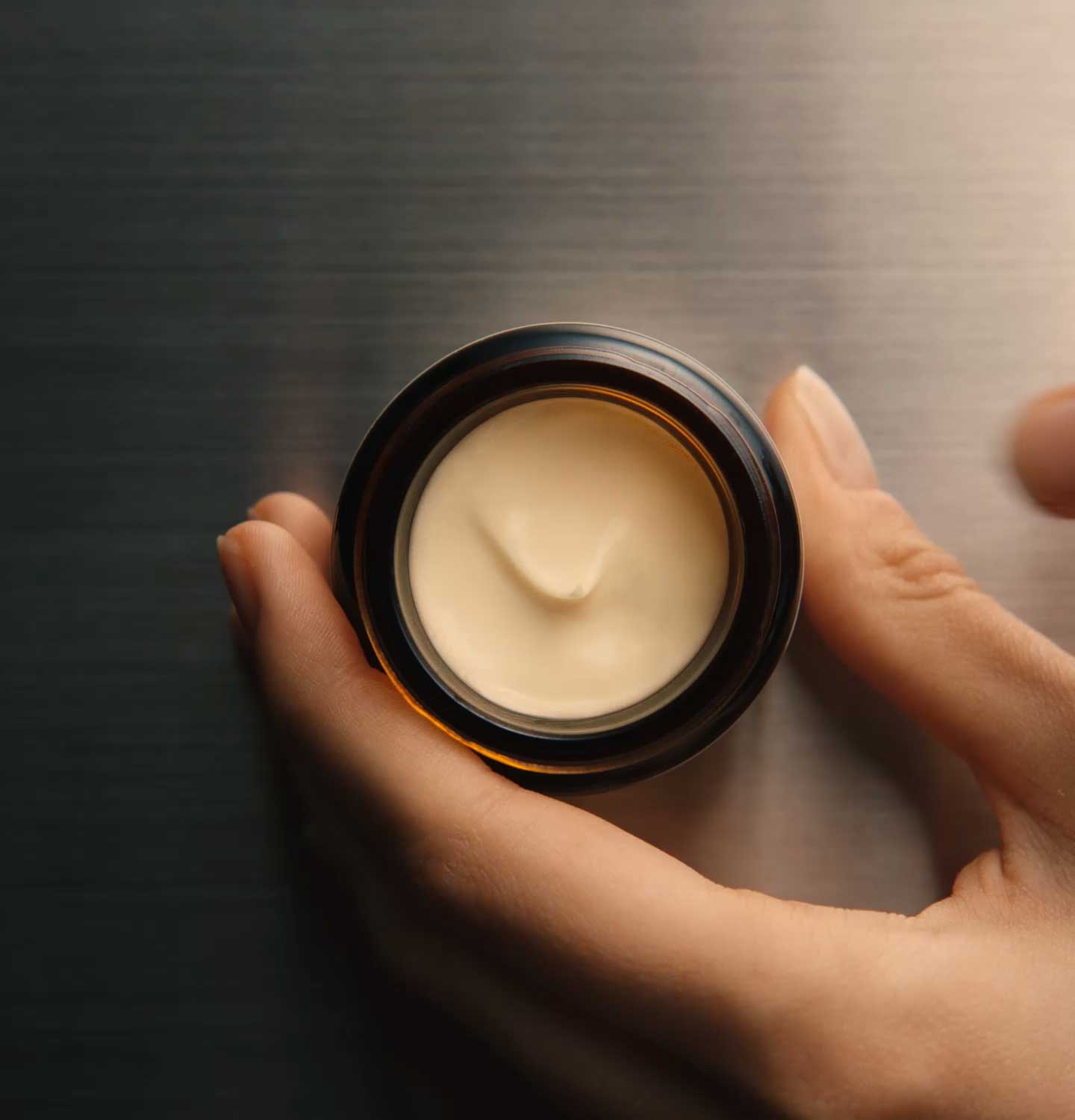 Hand holding an amber glass jar full of Camellia nut facial hydrating cream