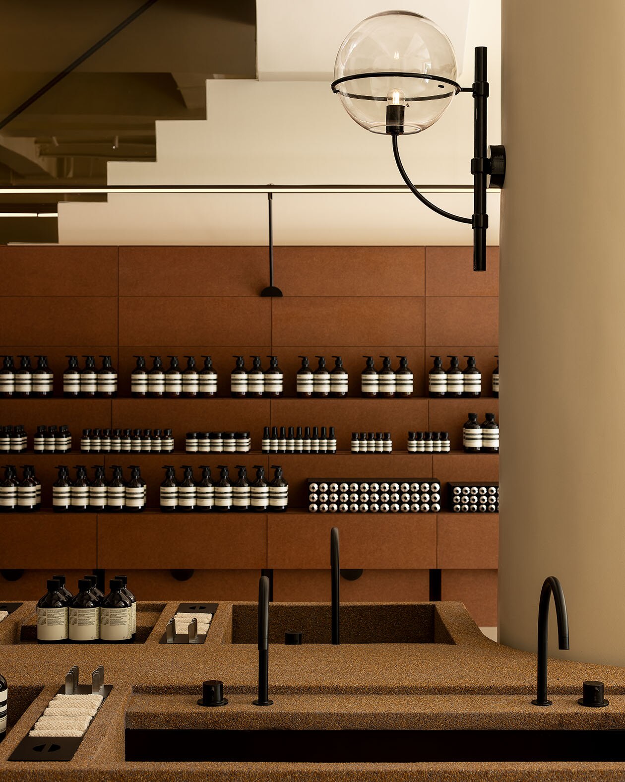 Pebbled finish with sink surfaces while Aesop products are at the tiered shelves.