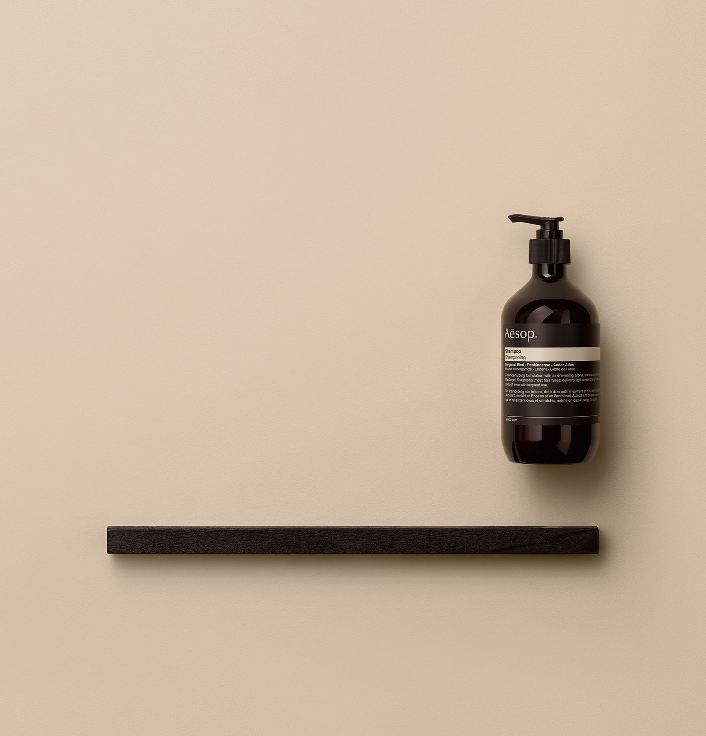 Amber pump bottle arranged alongside a dark wooden object on a pink textured surface.