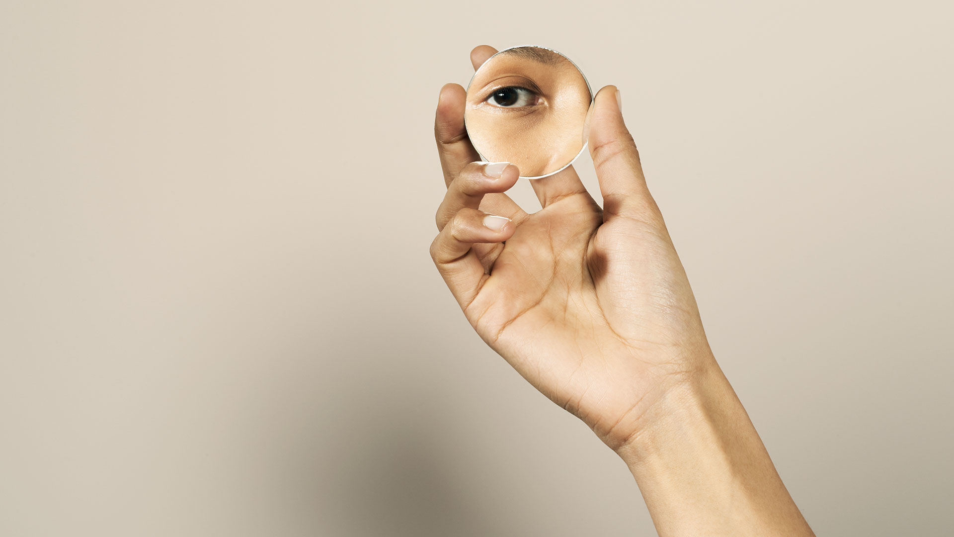 A hand holding a mirror reflecting her eye