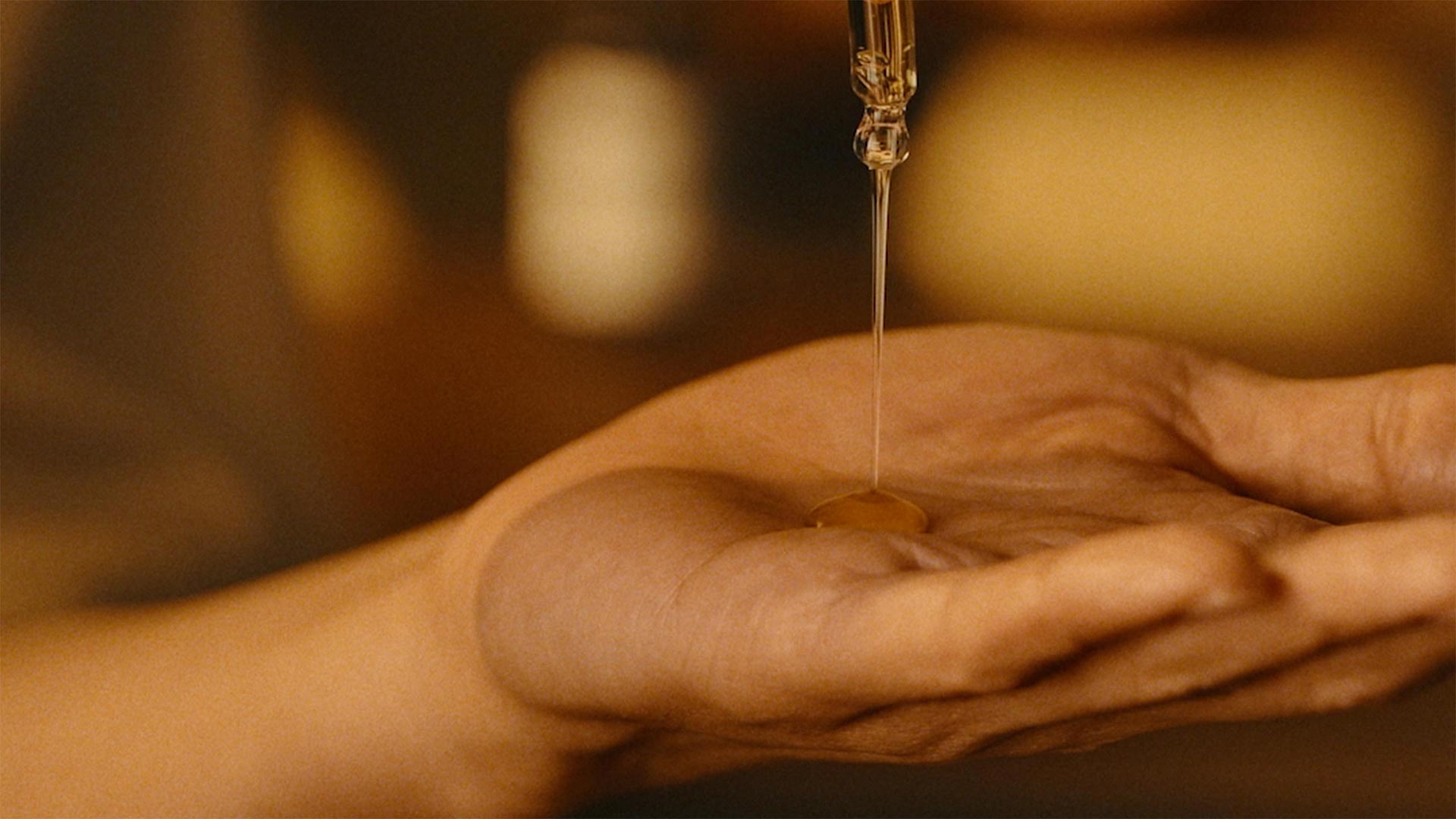 A hand holding a pipette dropper and squeezing a product on to another hand