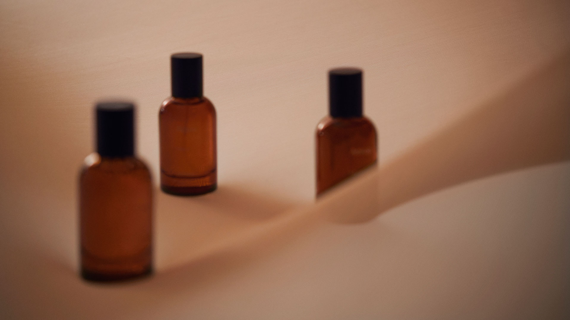 Three amber fragrance bottles nestled in layers earth-toned fabric.